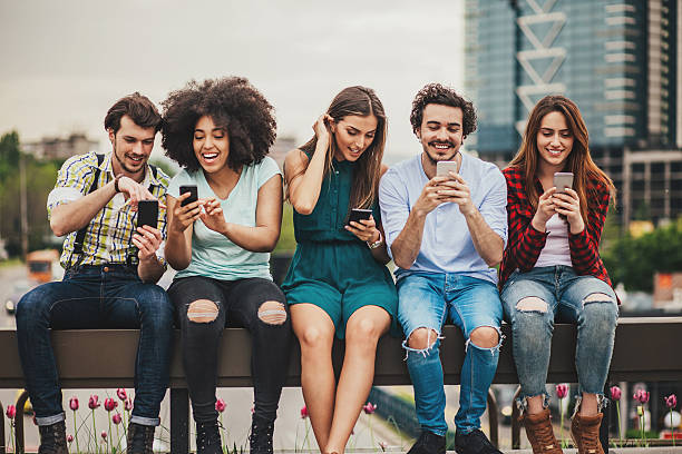 Multi-ethnic group of people sitting on an urban bridge text messaging and sharing smart phone content.