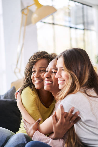 Three happy friends hugging smiling.Funny women together celebrating sitting on the living room sofa. High quality photo